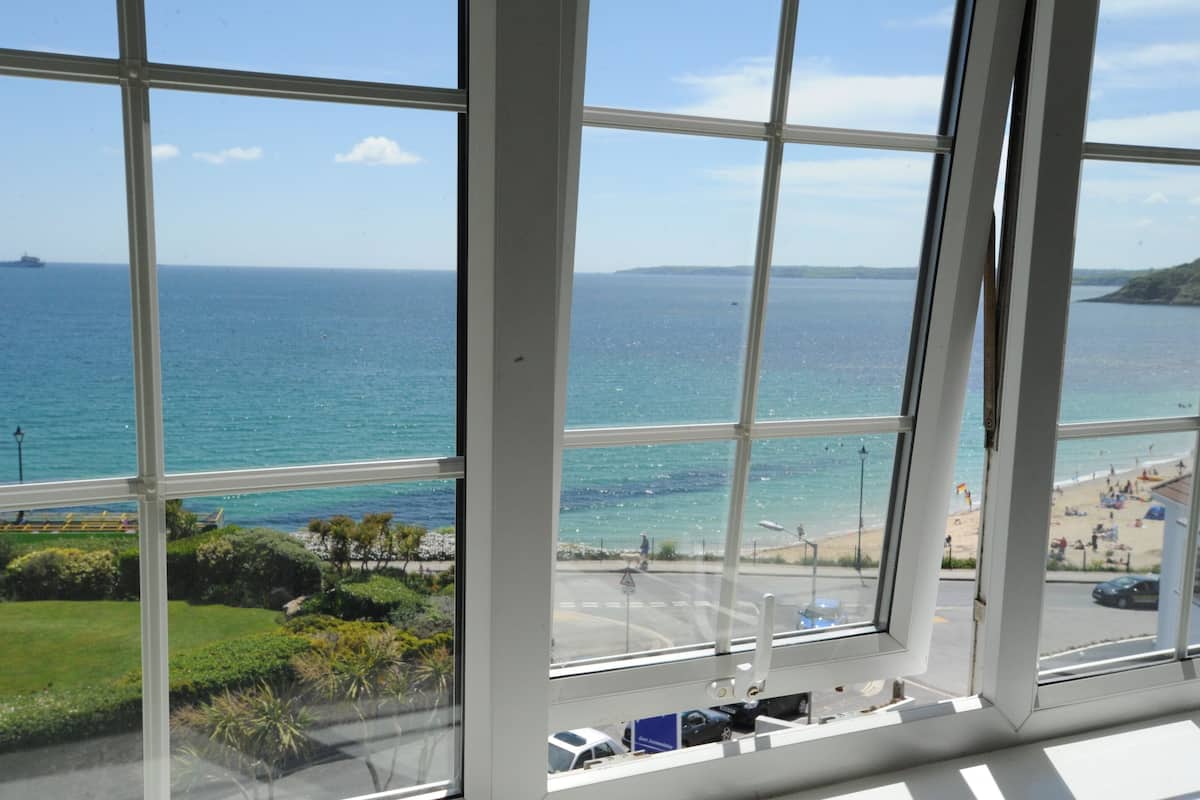 A view through large windows of a coastal area with a beach, a road, and a distant ship.