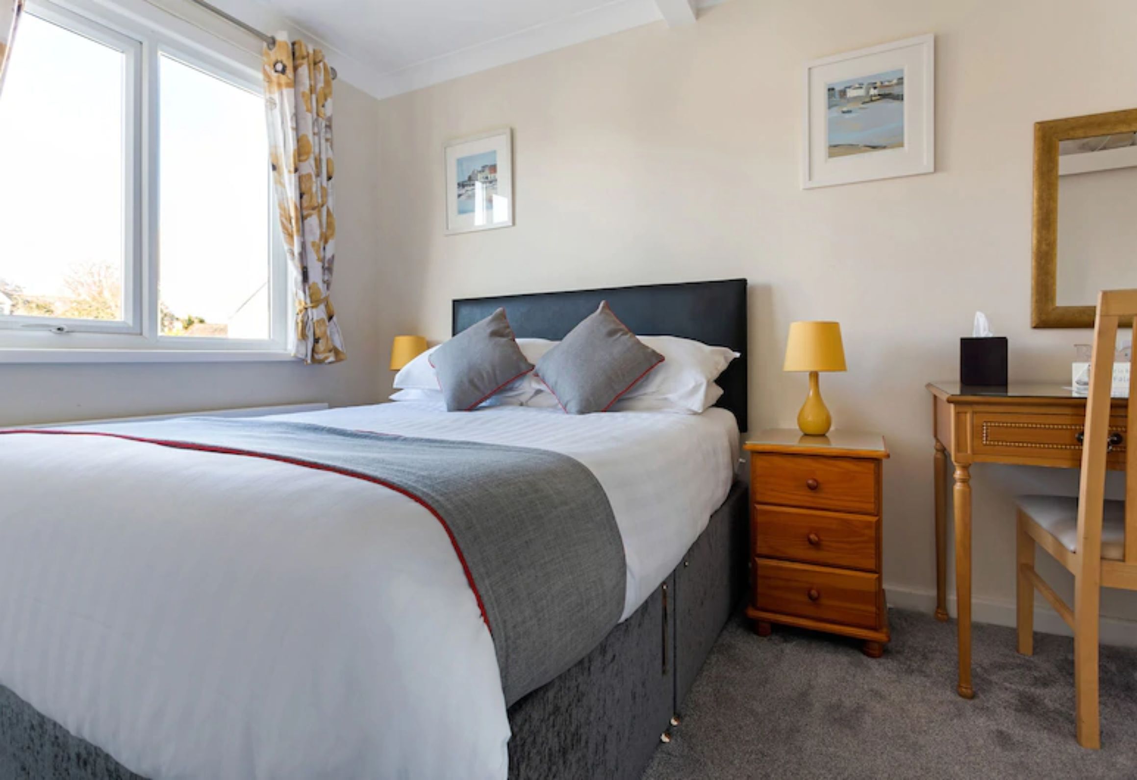 A neatly arranged bedroom with a bed, bedside tables, a desk, and a chair.