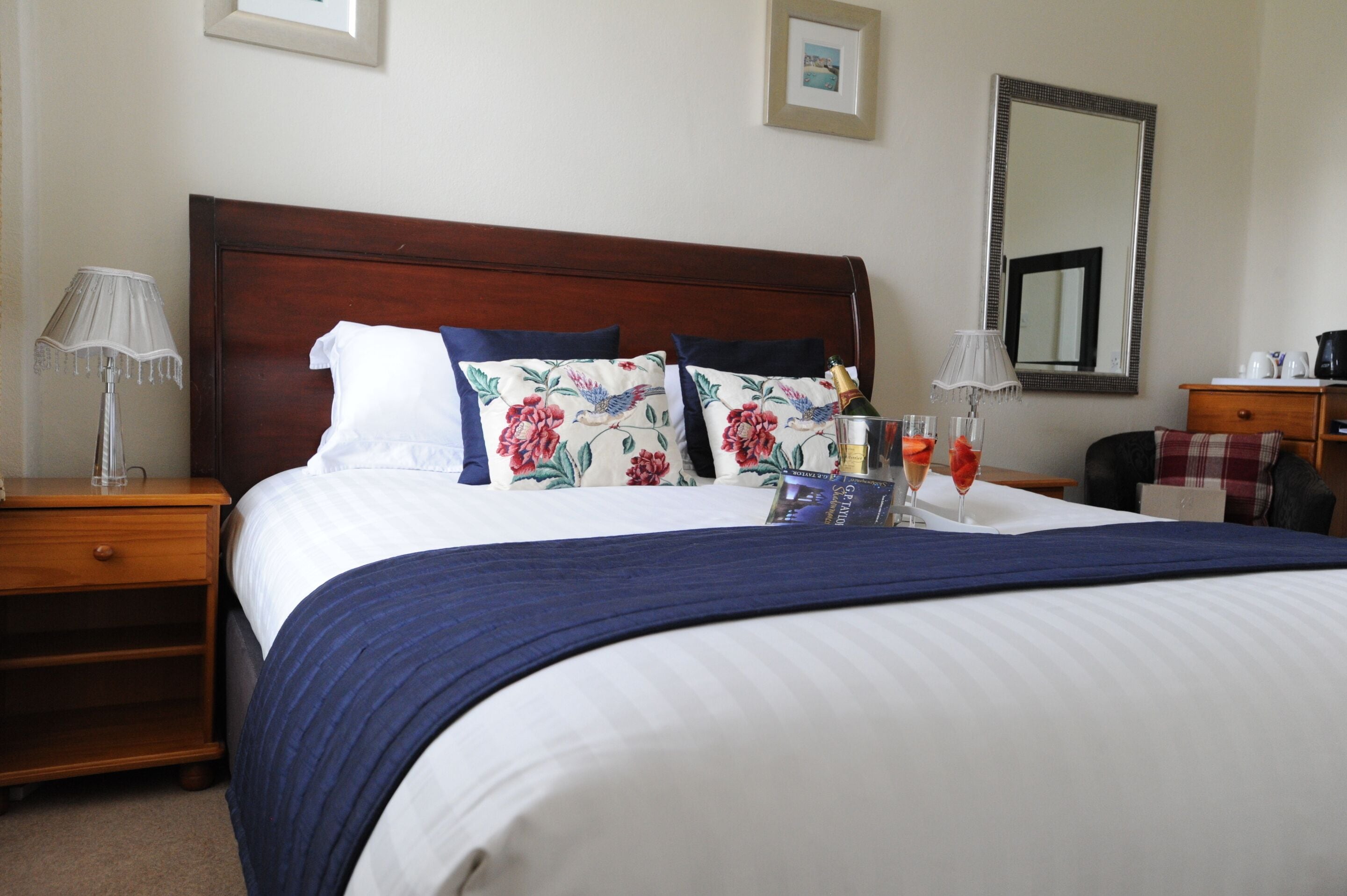 A neatly made bed with a blue and white striped bedspread, floral pillows, and a bottle of champagne.