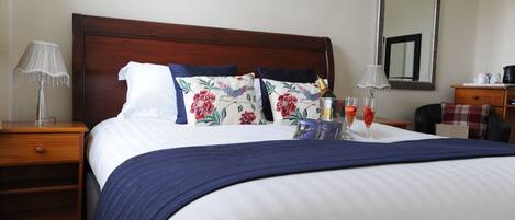 A neatly made bed with a blue and white striped bedspread, floral pillows, and a bottle of champagne.