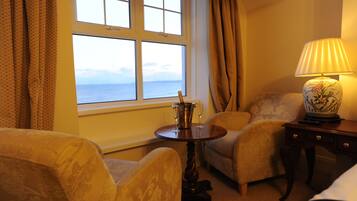 A room with a large window, two armchairs, a small table with a lamp, and a decorative vase.