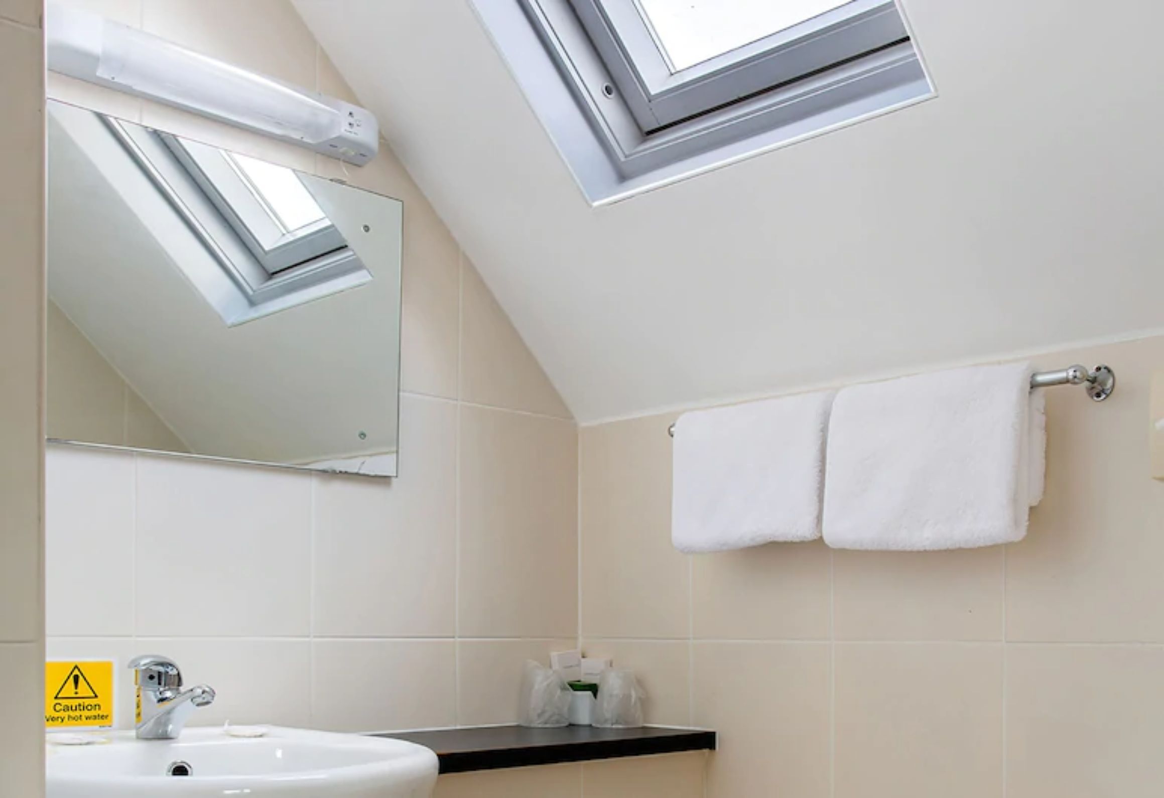A bathroom with a skylight, a sink, a towel rack, and a caution sign for hot water.