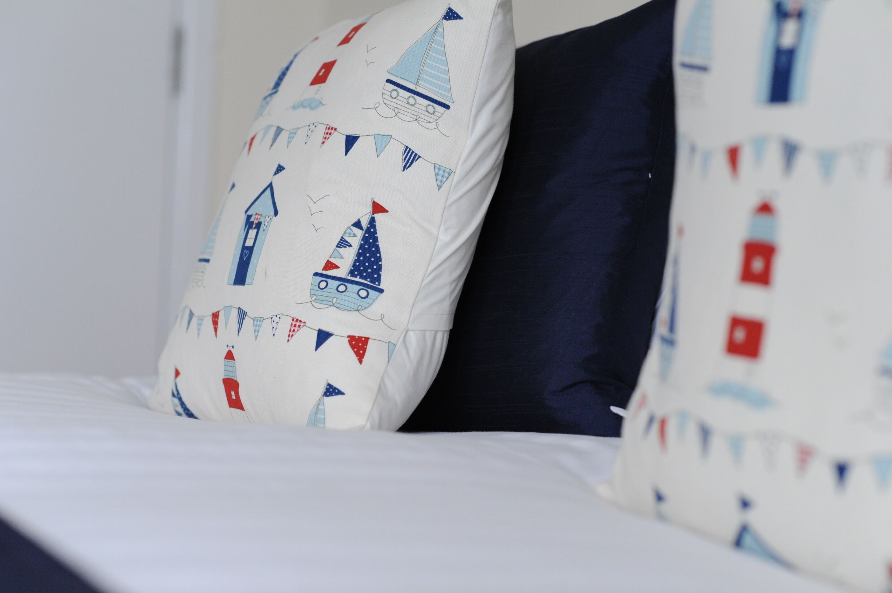 A bed with white bedding and two pillows, one with a nautical pattern and the other solid navy blue.