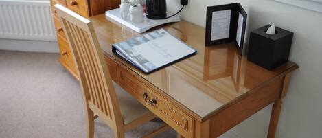 A wooden desk with a glass top, a coffee maker, a framed menu, and a tissue box.