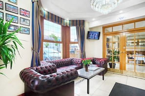 A hotel lobby with a leather sofa, a coffee table, a TV, and a sign indicating a breakfast room.