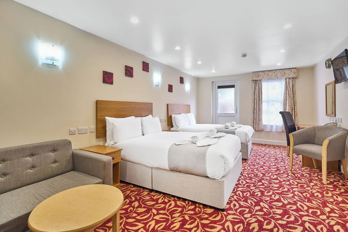A hotel room with two beds, a sofa, a chair, a small table, and a window with curtains.