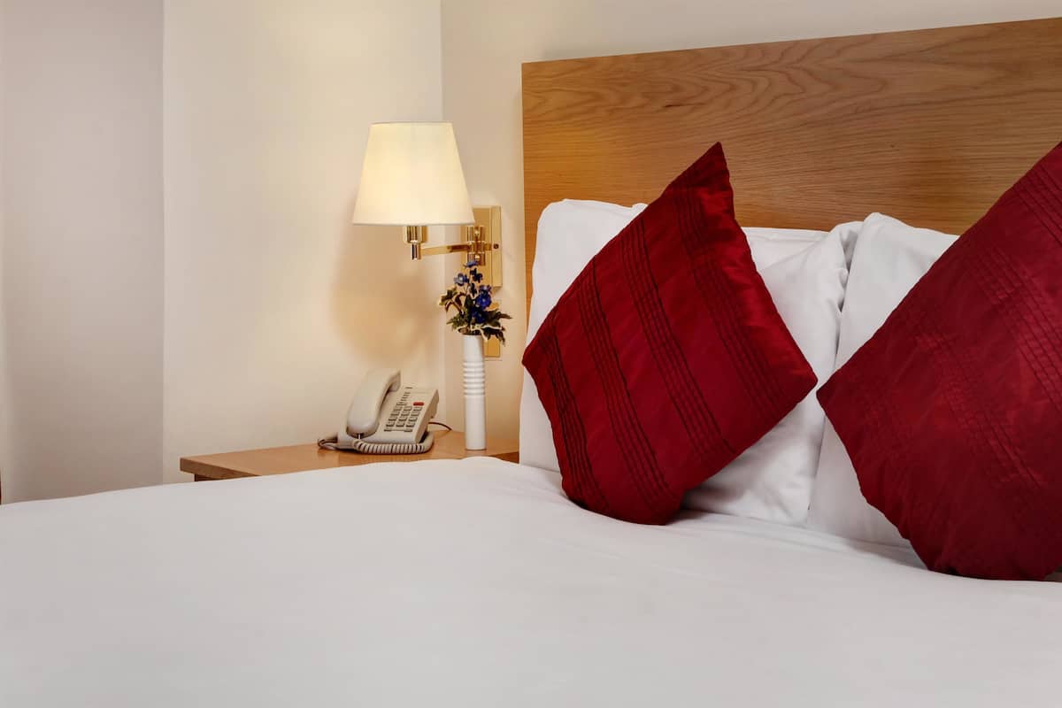 A neatly made bed with red and white pillows, a bedside lamp, and a telephone on a wooden nightstand.