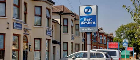 A Best Western hotel sign, a parked car, and a building with multiple windows and doors.