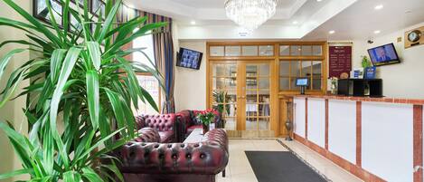 A reception area with a chandelier, a large potted plant, a red leather sofa, and a reception desk.