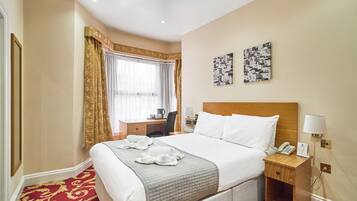A hotel room with a large bed, a desk, a chair, a lamp, and two wall art pieces.