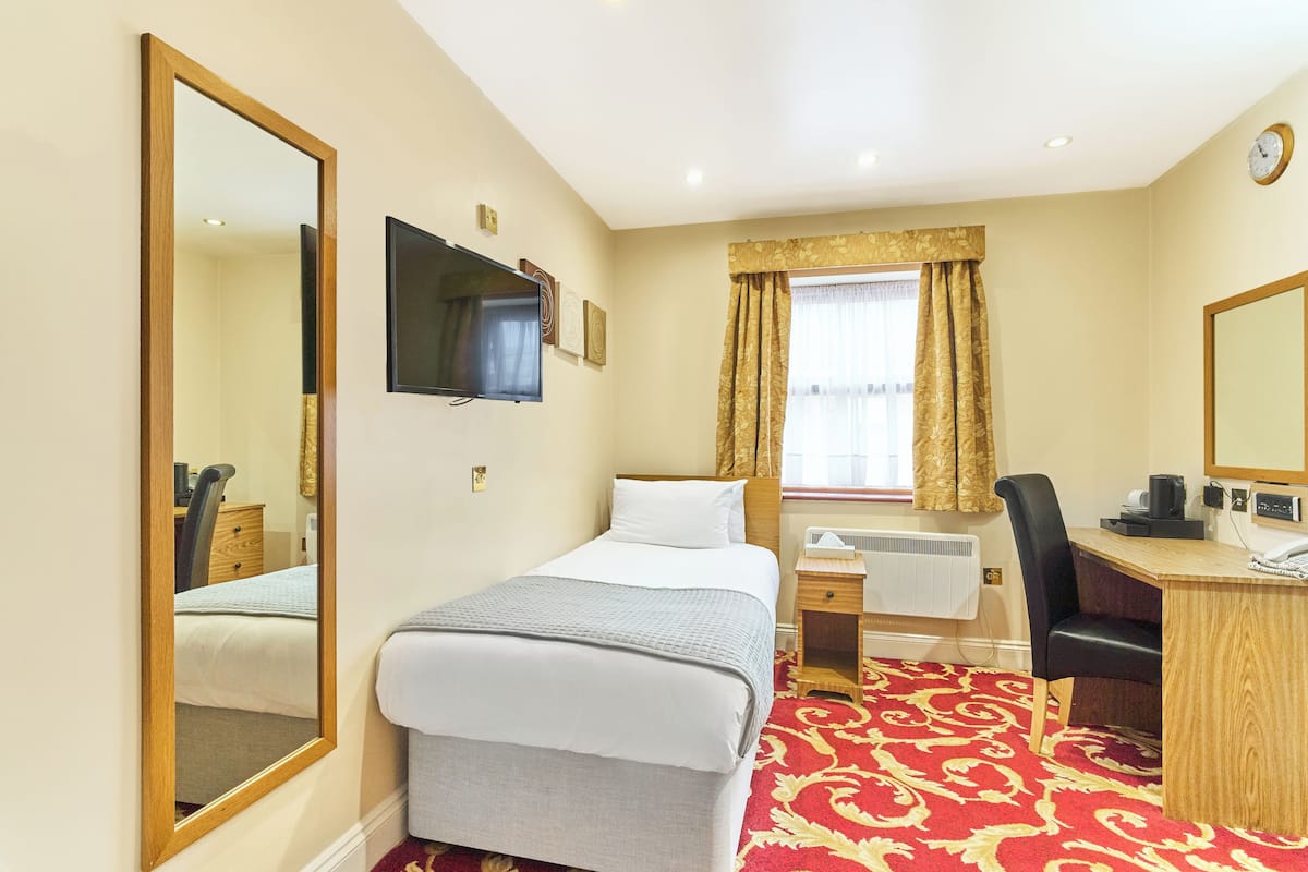 Ein Hotelzimmer mit Bett, Schreibtisch, Stuhl, Fernseher, einem Fenster mit Vorhängen und einer Wanduhr.