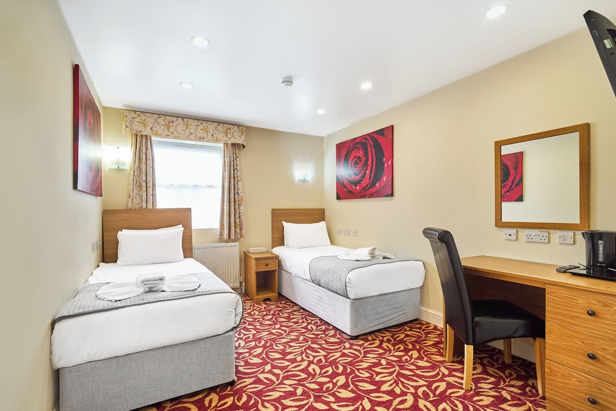 A hotel room with two beds, a desk, a chair, a window with curtains, and artwork on the walls.