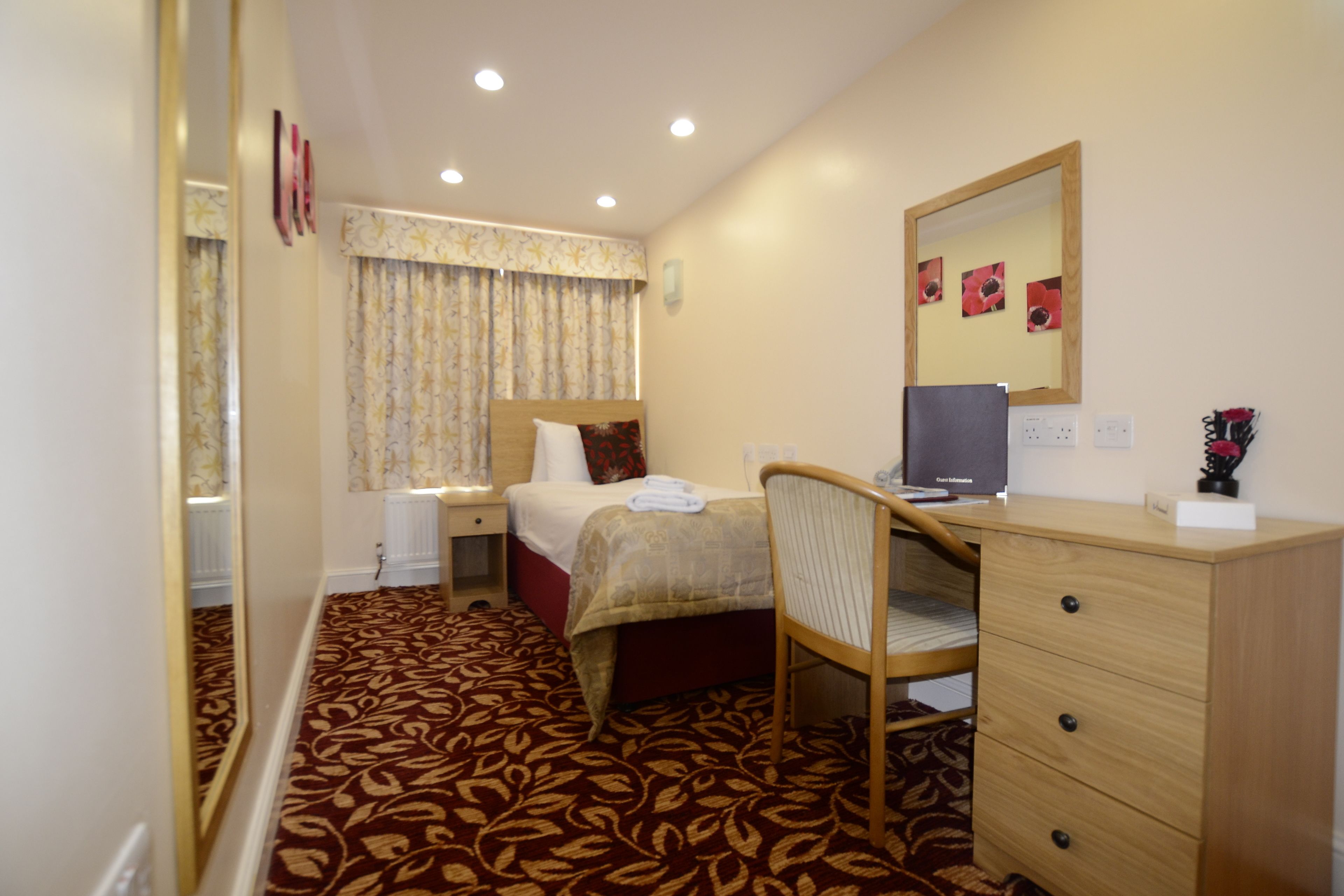 Una camera d'albergo con un letto, una scrivania, una sedia, un comò, uno specchio e un pavimento con moquette.