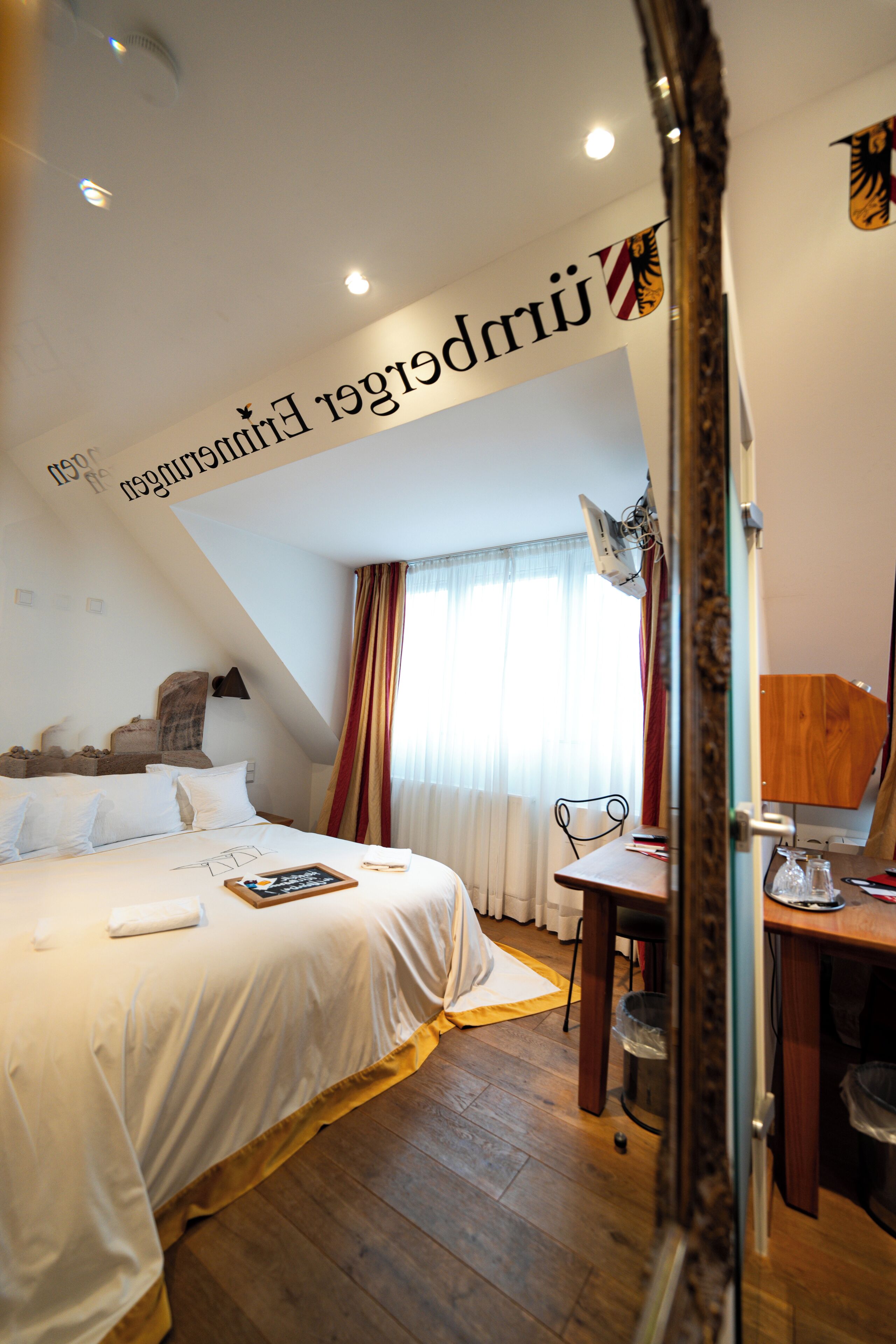 A hotel room with a bed, a desk, a chair, a lamp, and a mirror.