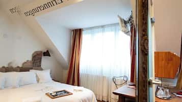A hotel room with a bed, a desk, a chair, a lamp, and a mirror.