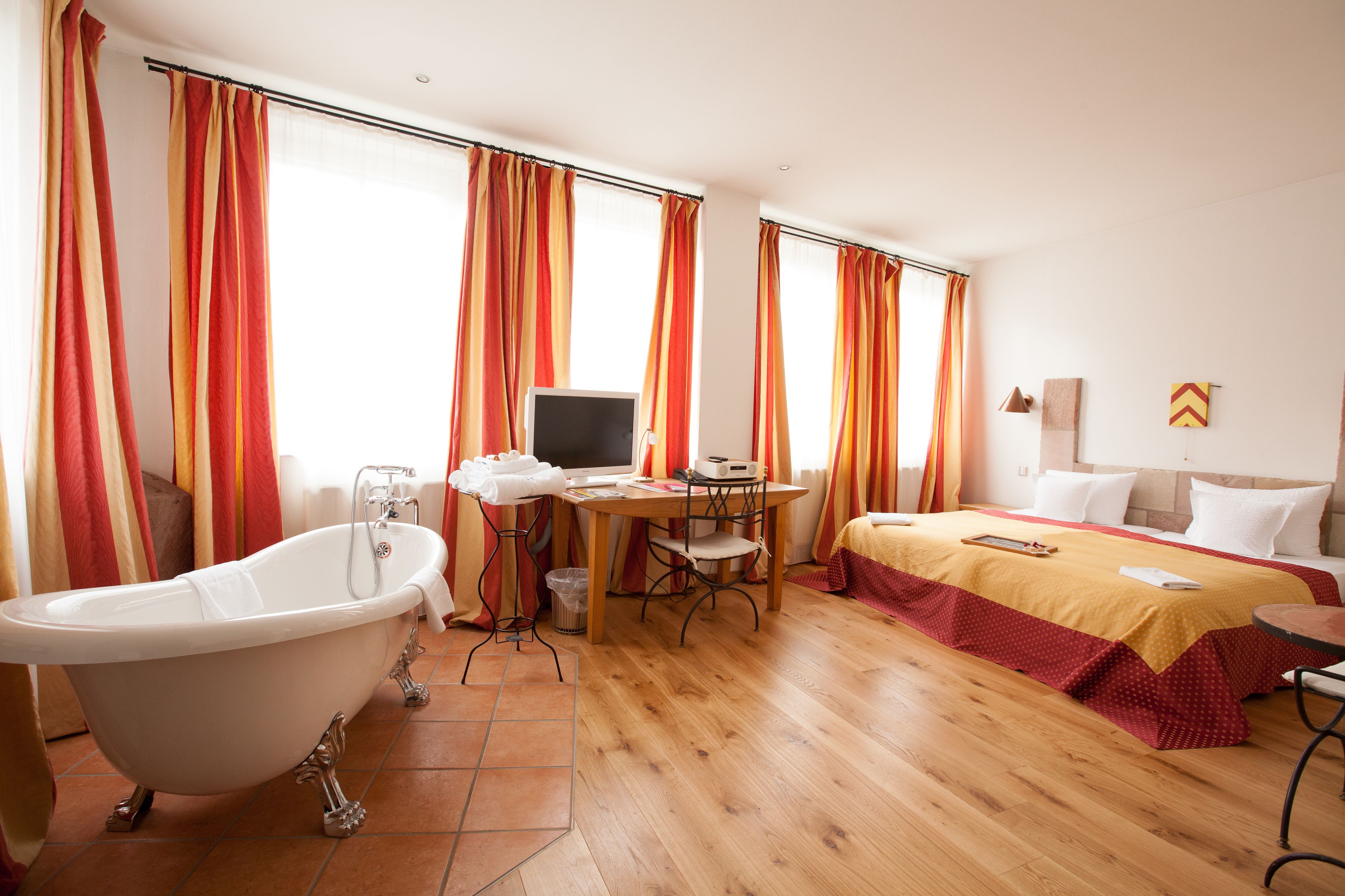 A hotel room with a bathtub, a desk with a computer, a bed, and a window with curtains.