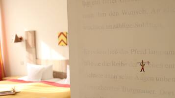 Quarto de hotel com uma cama, uma mesa redonda pequena e uma parede com texto e ilustrações.