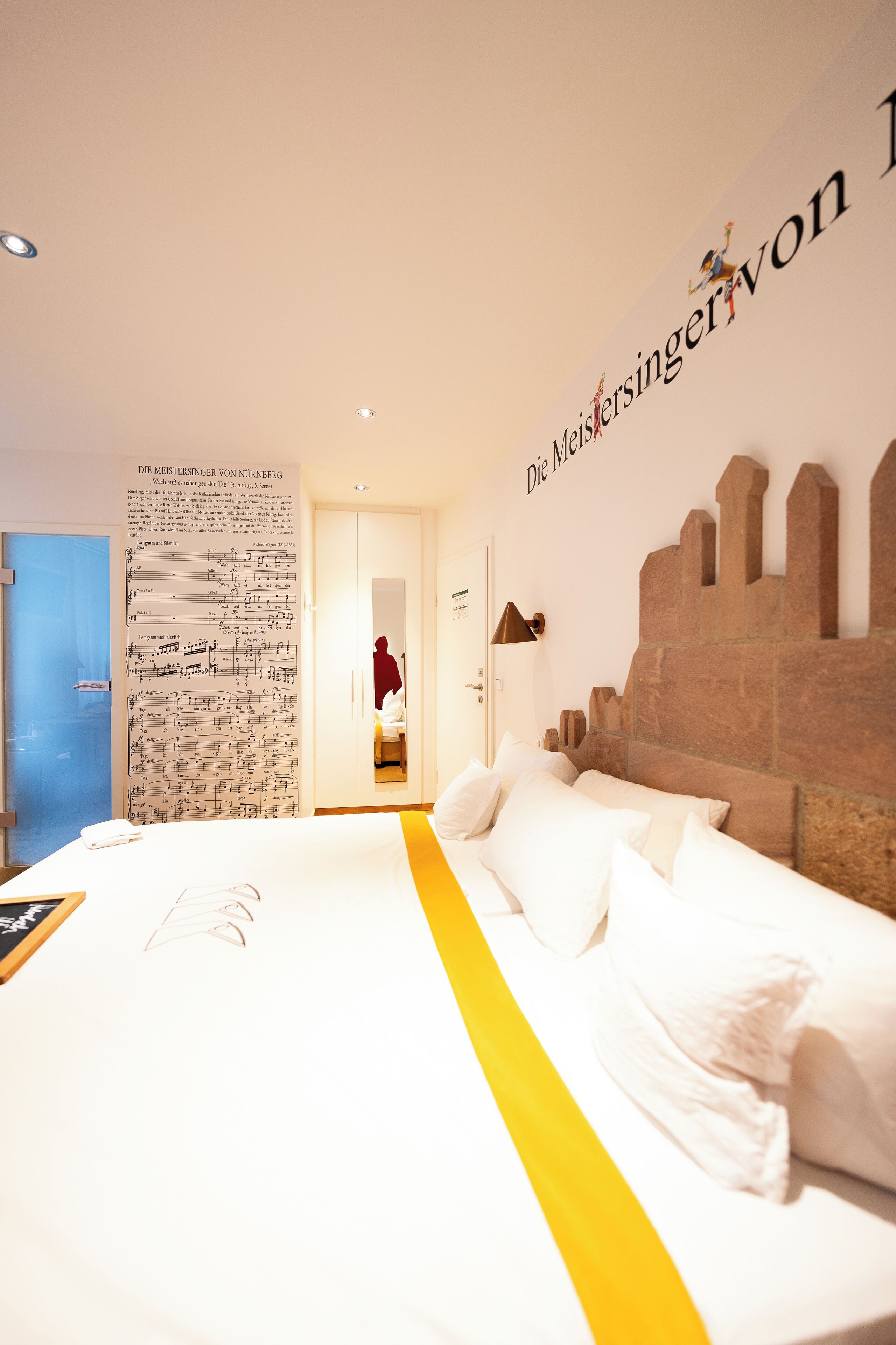 A hotel room with a large bed, a wall with a musical score, and a stone headboard.