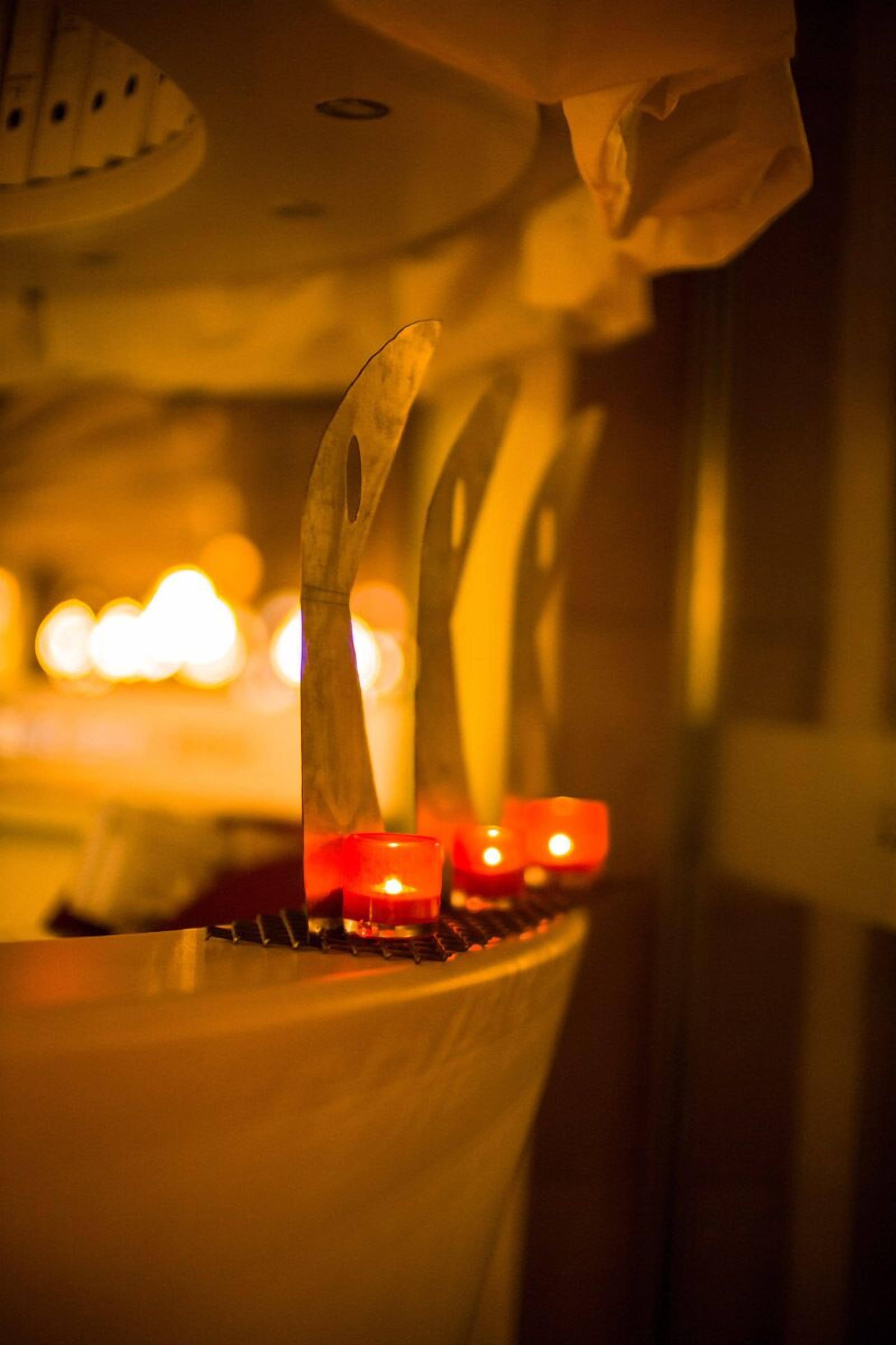 A close-up of a candle holder with a lit candle, a spoon, and a spoon resting on a surface.
