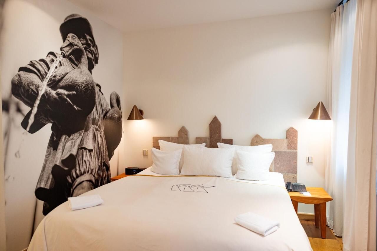 Una habitación de hotel con una cama grande, un cabecero de motivos geométricos, lámparas de noche y un mural en la pared.