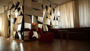 Una sala de estar moderna con un diseño geométrico en la pared, un sillón rojo, una mesa de centro de madera y un sofá.