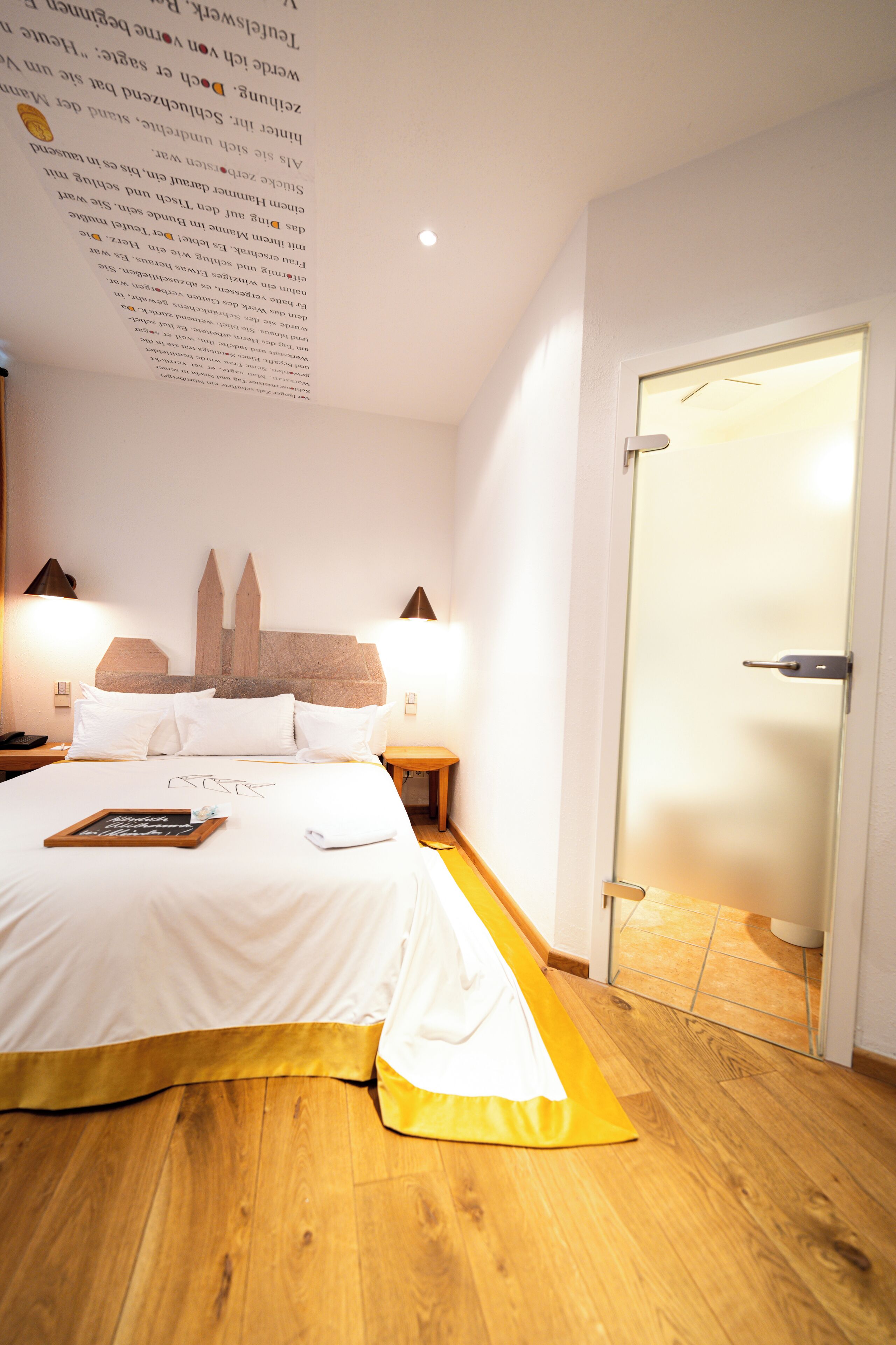 A neatly made bed with white linens, a bedside table with a lamp, and a wooden headboard.