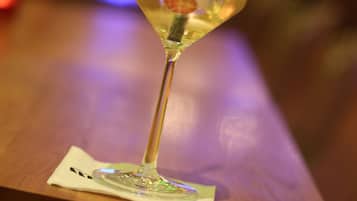A glass of cocktail on a wooden bar counter with a metal ring.