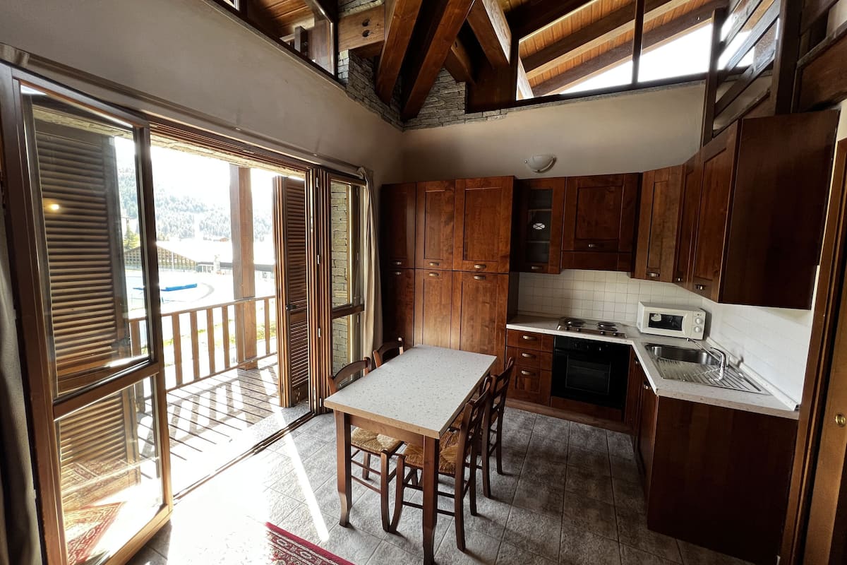 A kitchen with wooden cabinets, a white countertop, a dining table with chairs, and a view through a sliding glass door.