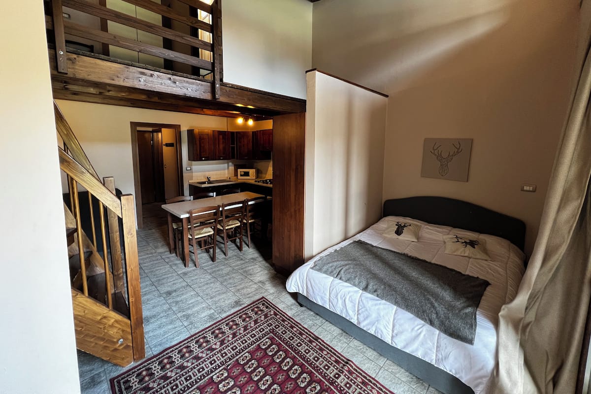 A bedroom with a bed, a desk, and a kitchen area.