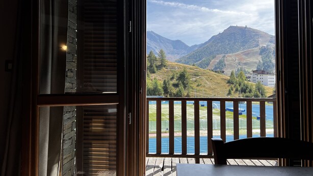 Quarto com vista para montanhas, varanda com corrimão e uma mesa.