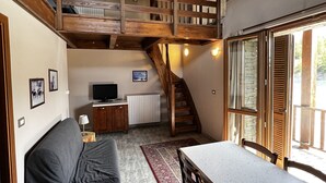 Um quarto em estilo loft com escada de madeira, mesa de jantar, sofá e televisão.