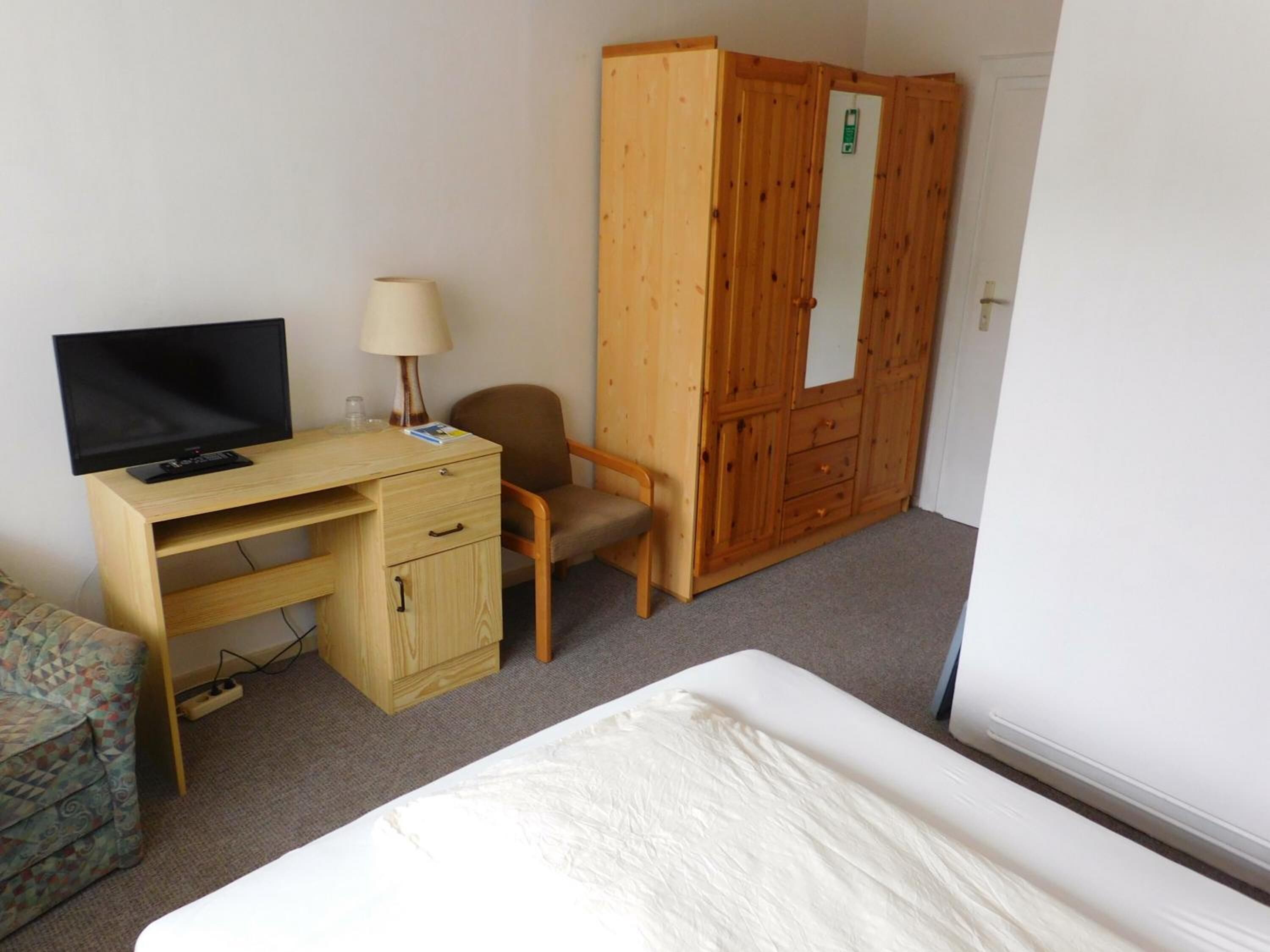 A room with a wooden desk, a television, a chair, a wardrobe, and a bed.