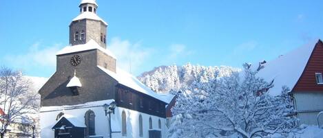 A church with a clock tower, surrounded by snow-covered trees and buildings.