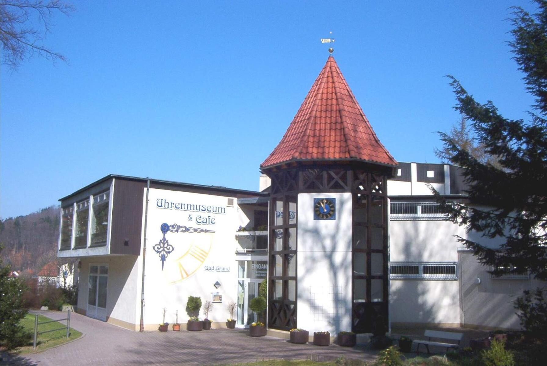 Ein Gebäude mit rotem Ziegeldach, einer Uhr und einem Schild mit der Aufschrift 'Uhrenmuseum & Cafe'.