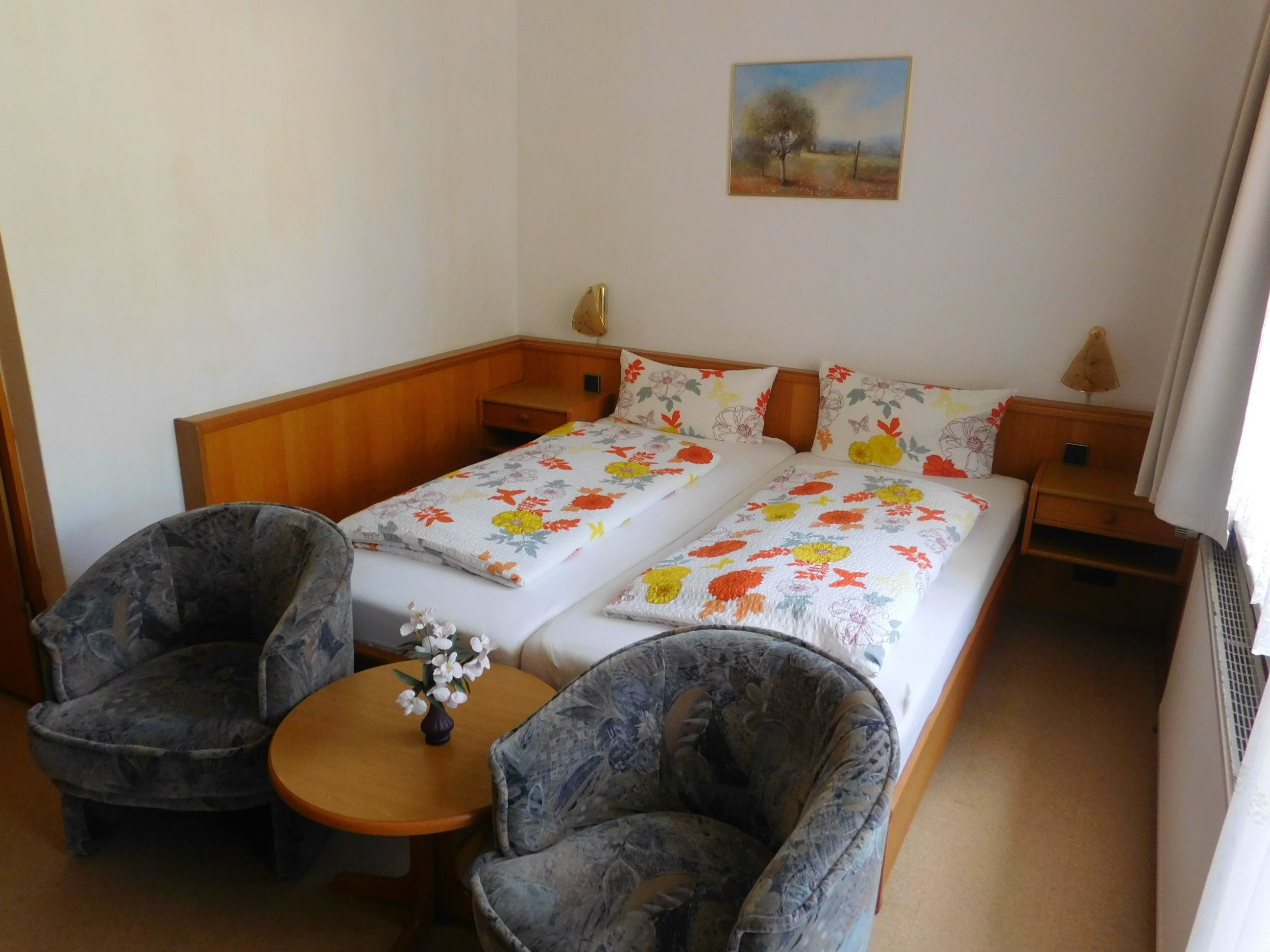 Een slaapkamer met een tweepersoonsbed, twee stoelen, een kleine tafel en een schilderij aan de muur.