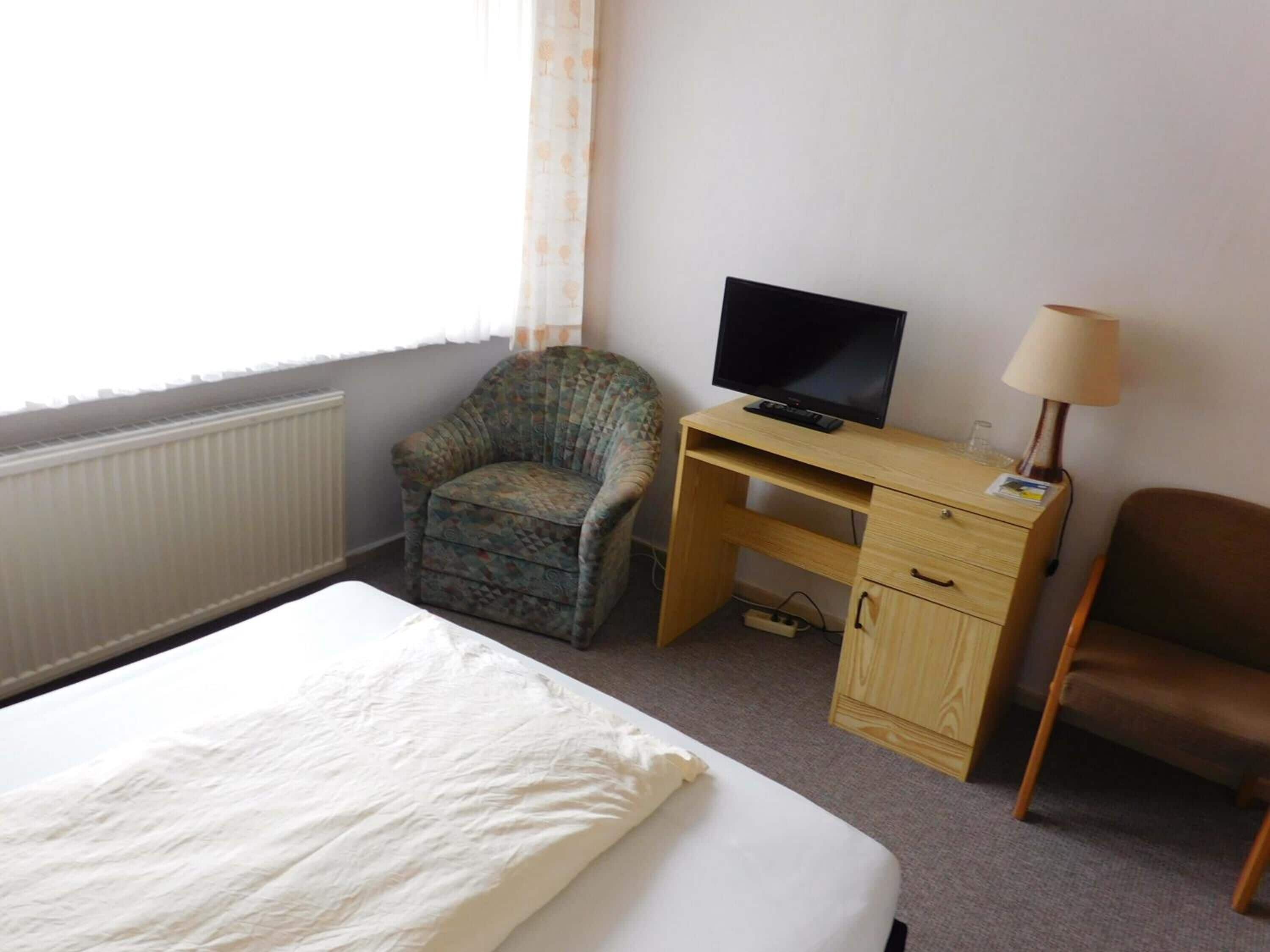 A bedroom with a bed, a desk with a television, a chair, and a lamp.