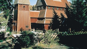 A church with two prominent spires and a smaller tower, surrounded by trees and a fence.