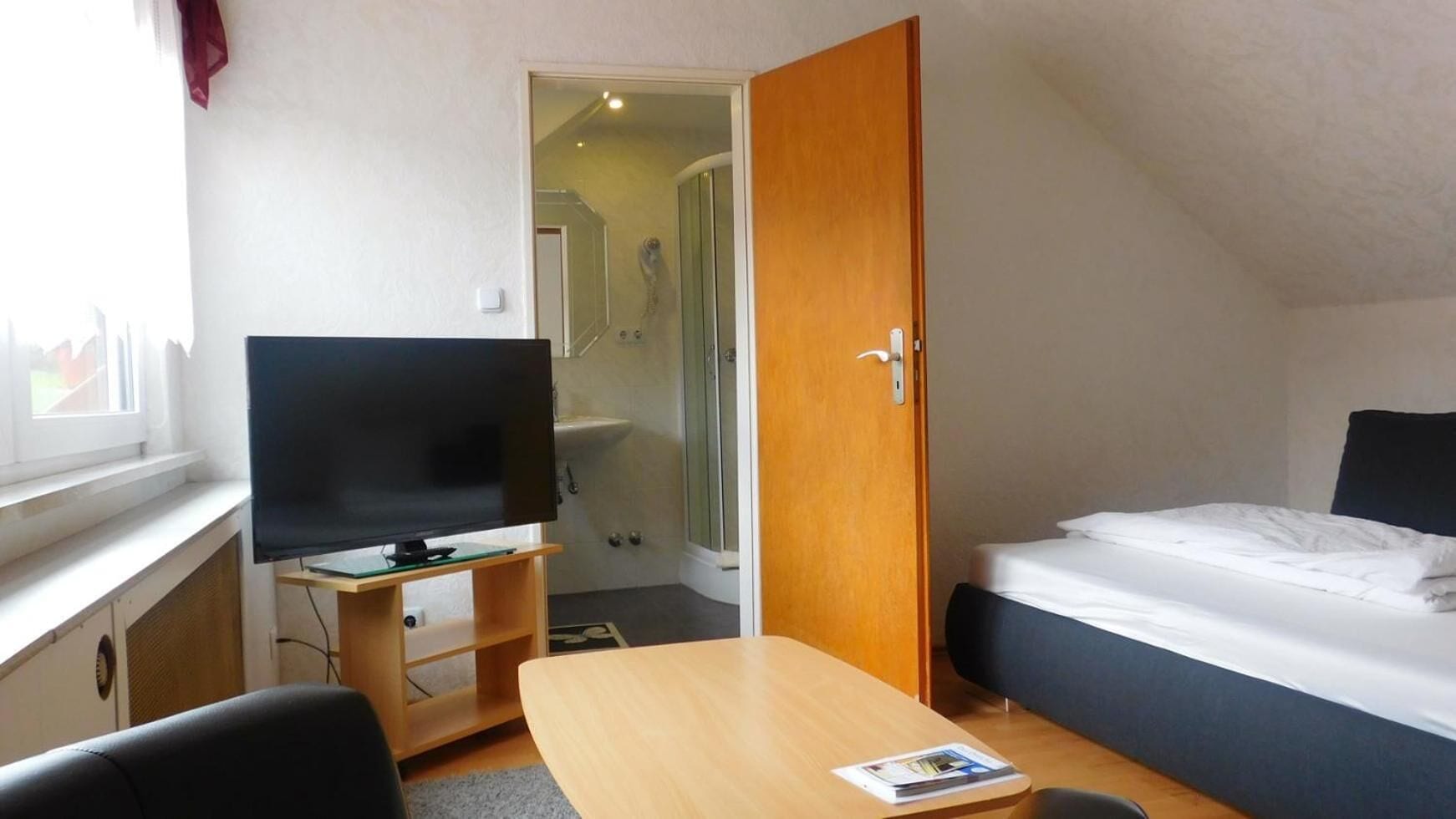 Ett hotellrum med en säng, en tv på ett träställ, ett litet bord och en dörr som leder till ett badrum.