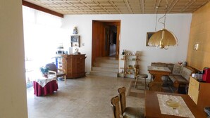 A spacious living area with a dining table, chairs, a wooden cabinet, and a staircase leading to another room.