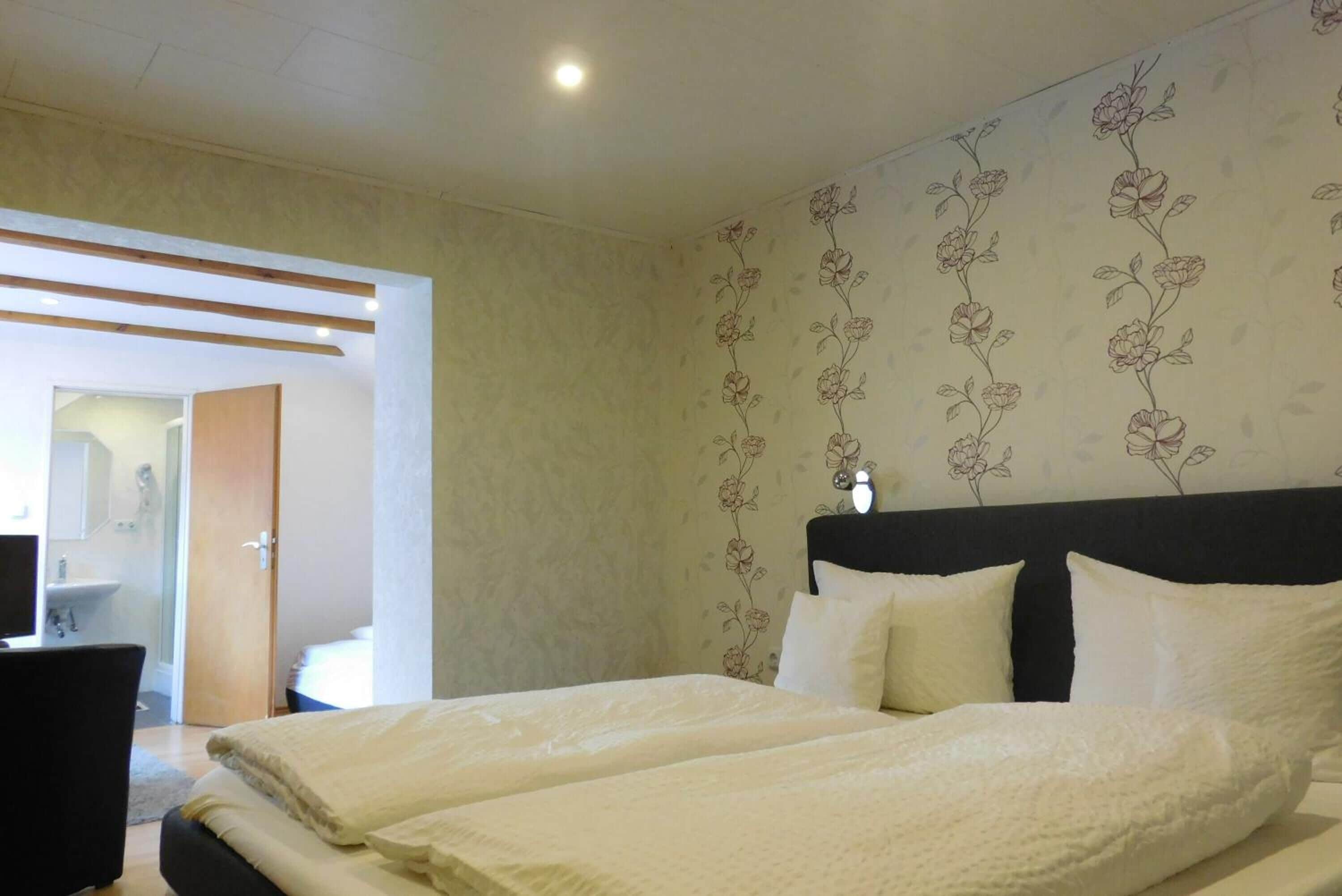 Une chambre avec un grand lit, une table de chevet et un miroir. Une porte donne accès à une salle de bain.