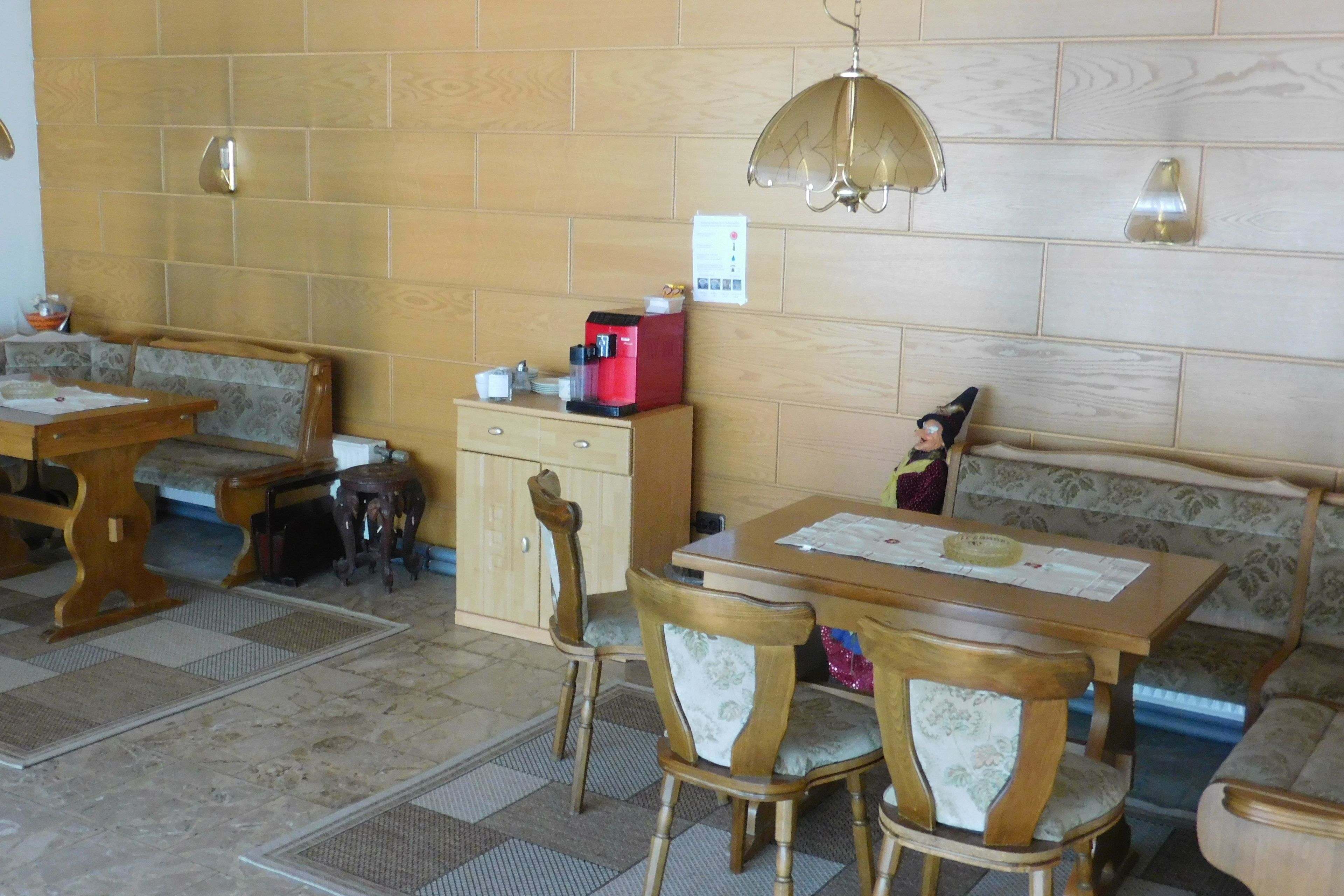 Una zona de menjador amb taula de fusta, cadires, un banc i una màquina de cafè.