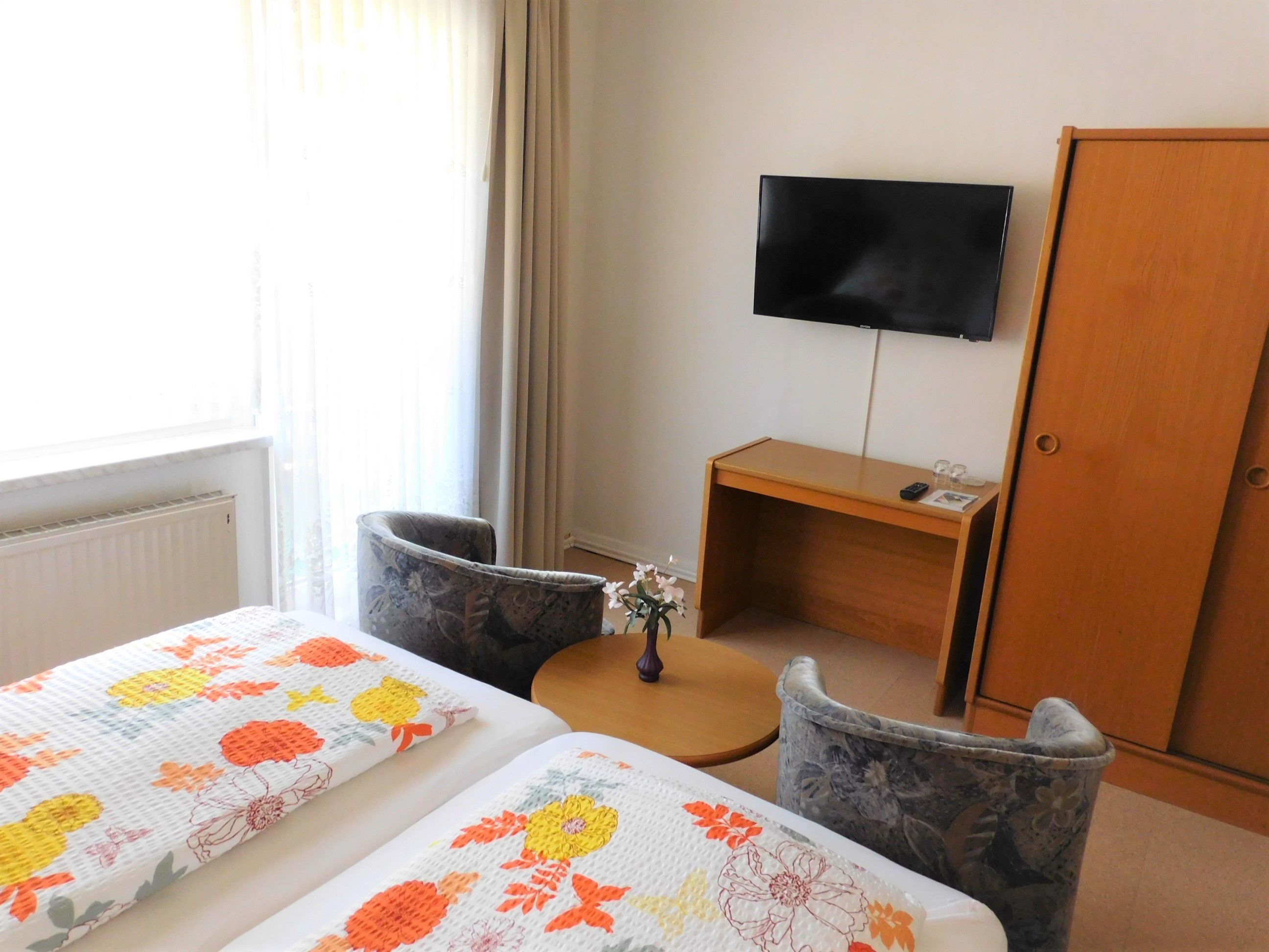 A hotel room with two beds, a desk, a chair, a TV, and a wardrobe.