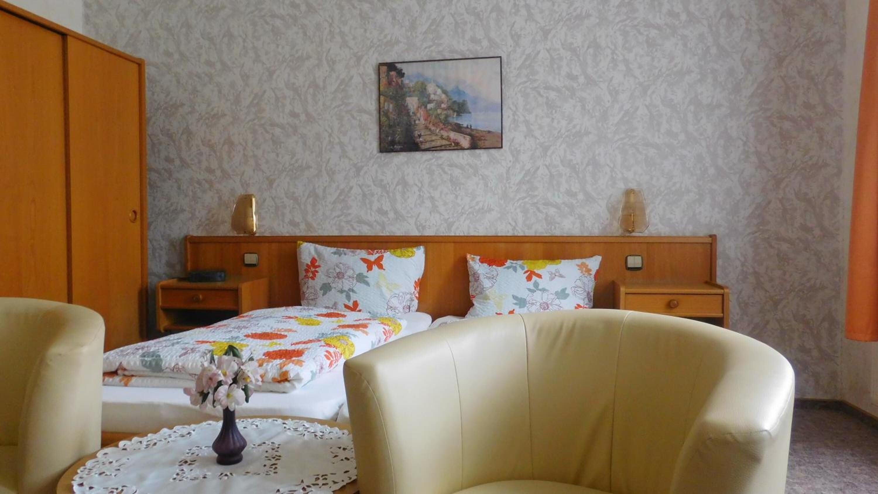 Une chambre d’hôtel avec un lit, deux tables de chevet, une tête de lit en bois, un tableau au mur et un vase avec des fleurs sur la table d’appoint.