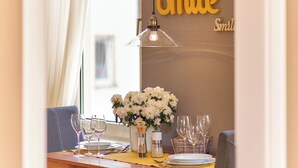Un comedor con una mesa de madera dispuesta para dos, un jarrón con flores blancas y una pared con la palabra "Smile" repetida.