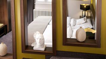A hotel room with a bed, a bedside lamp, a framed mirror, and a sculpture on the nightstand.
