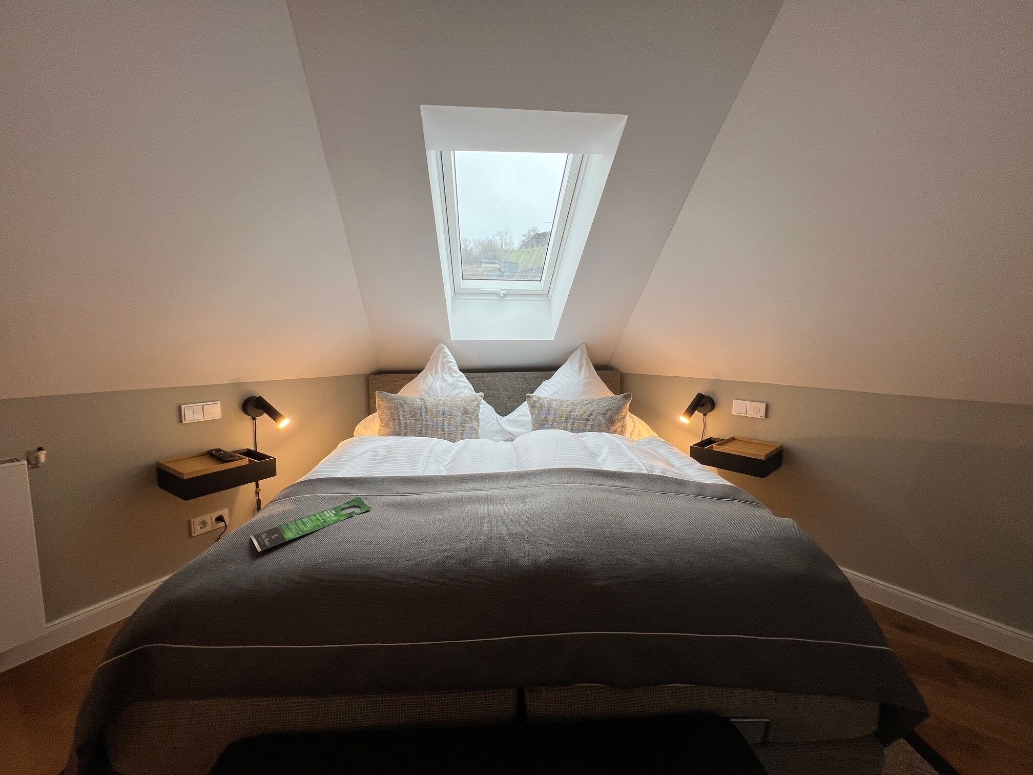 Ein Schlafzimmer mit Dachfenster, einem Bett mit Kissen, Nachttischen und einer Fernbedienung auf dem Bett.