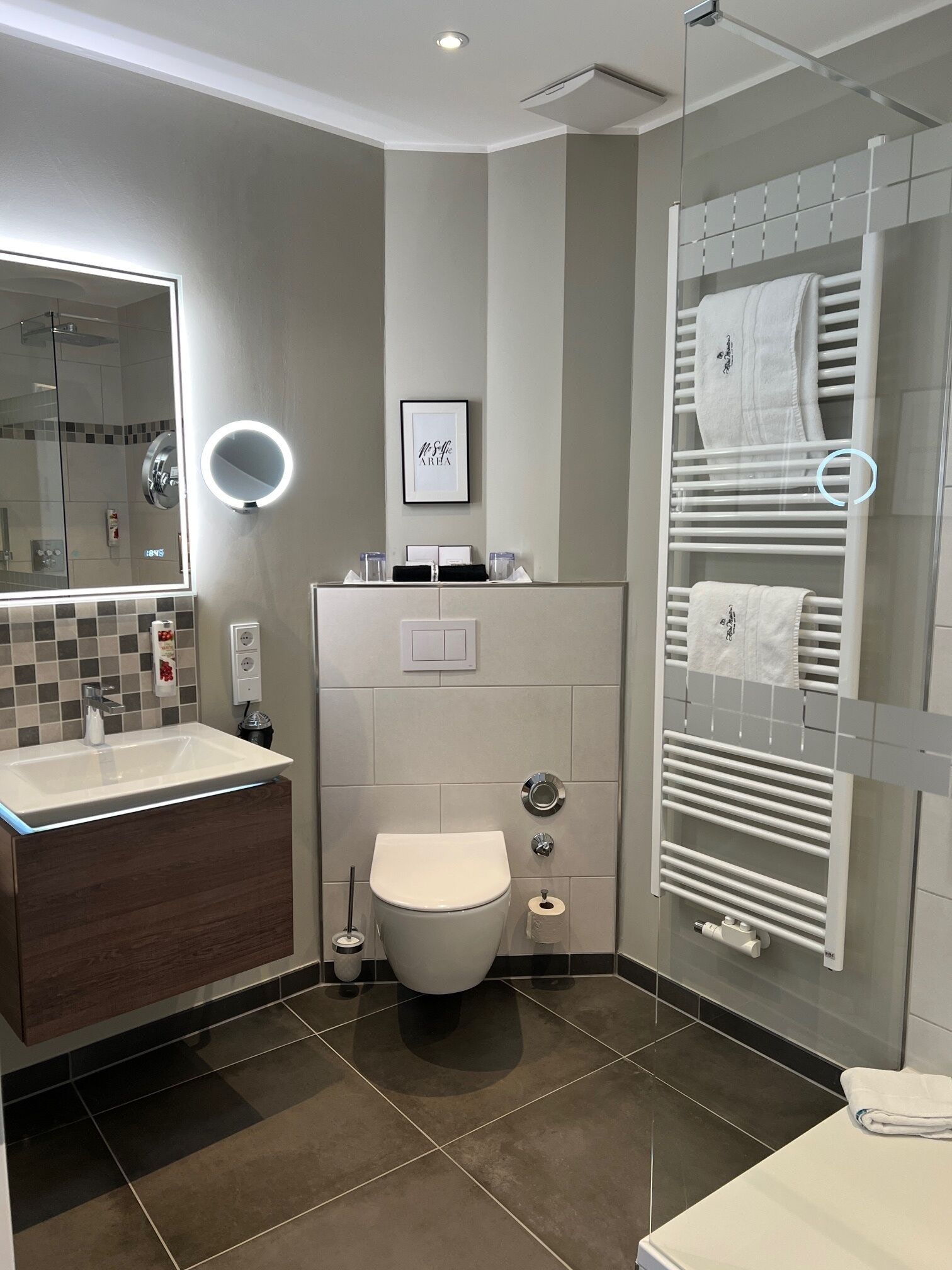 A modern bathroom with a large mirror, a toilet, a sink, and a towel rack.