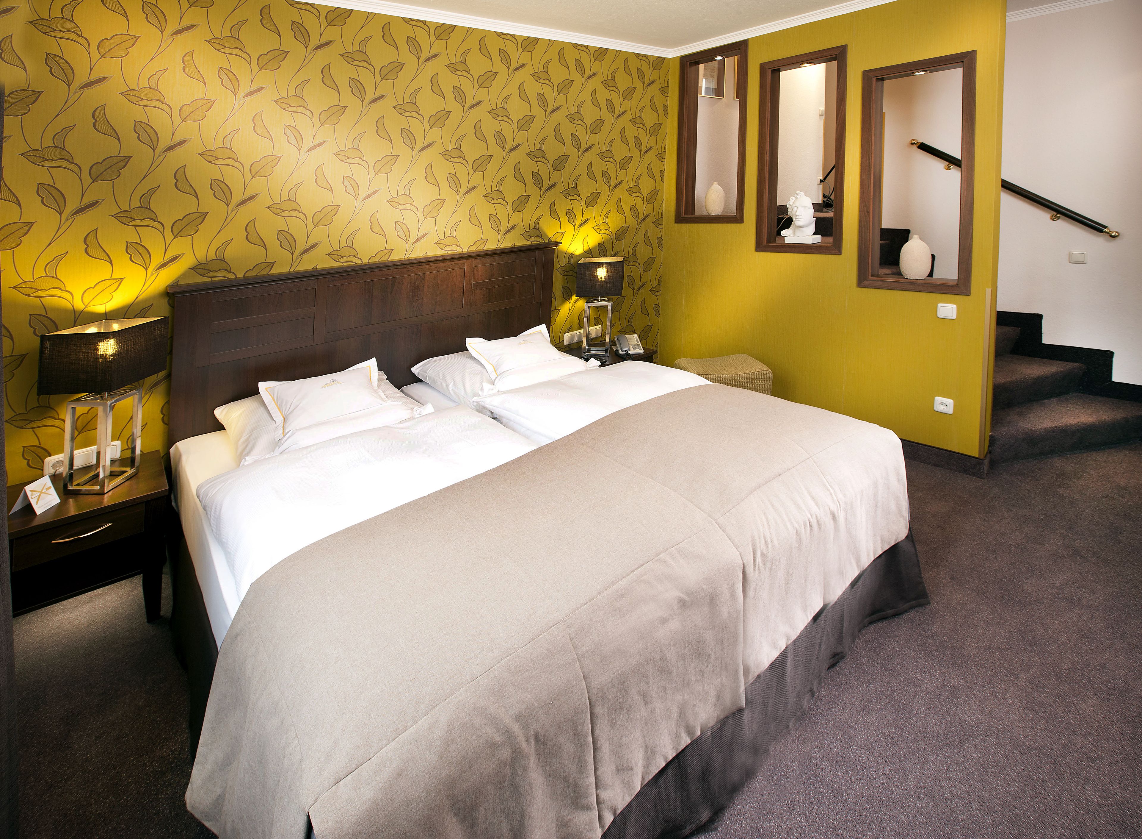 A hotel room with a large bed, two bedside tables with lamps, a mirror, and a staircase.