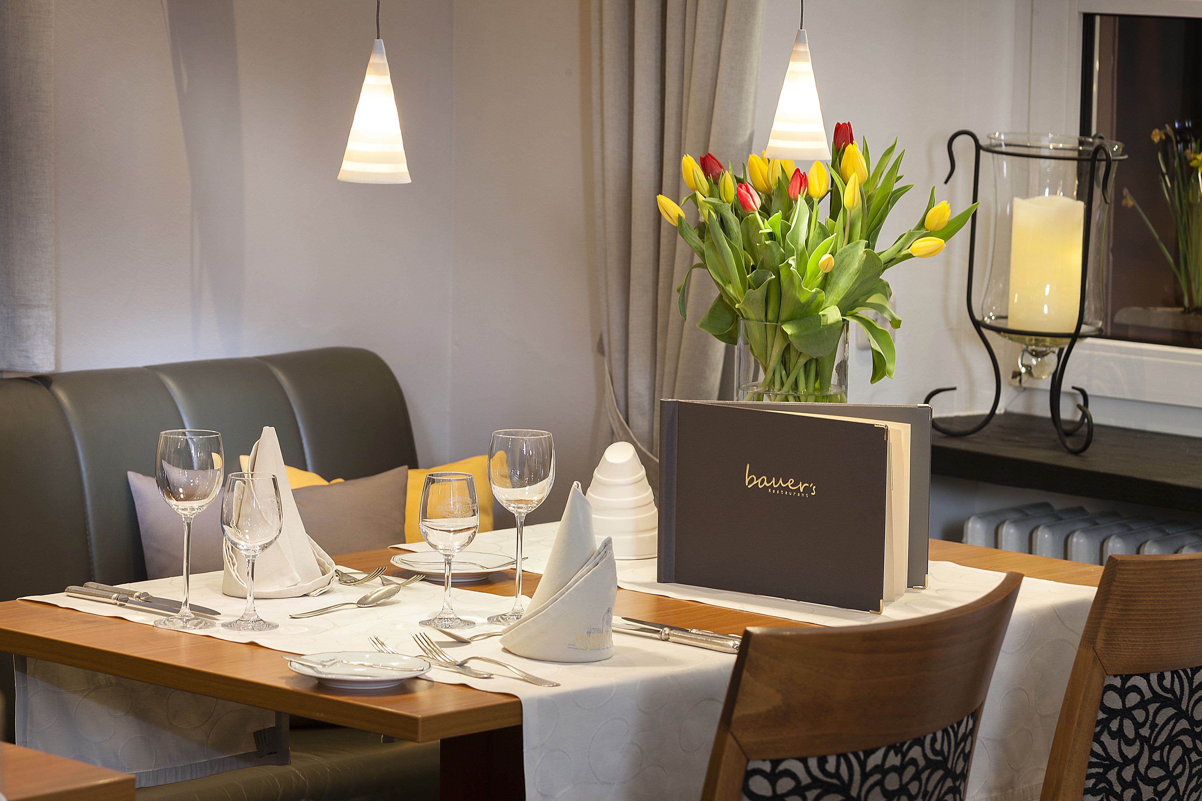 A dining table set with white tableware, a vase of tulips, and a candle holder.