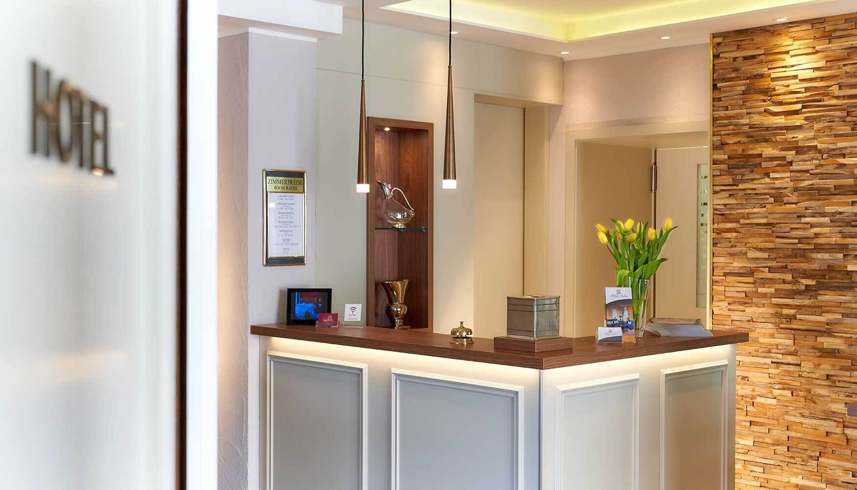 A hotel reception area with a wooden reception desk, a framed sign above it, and a wall with a wooden texture.